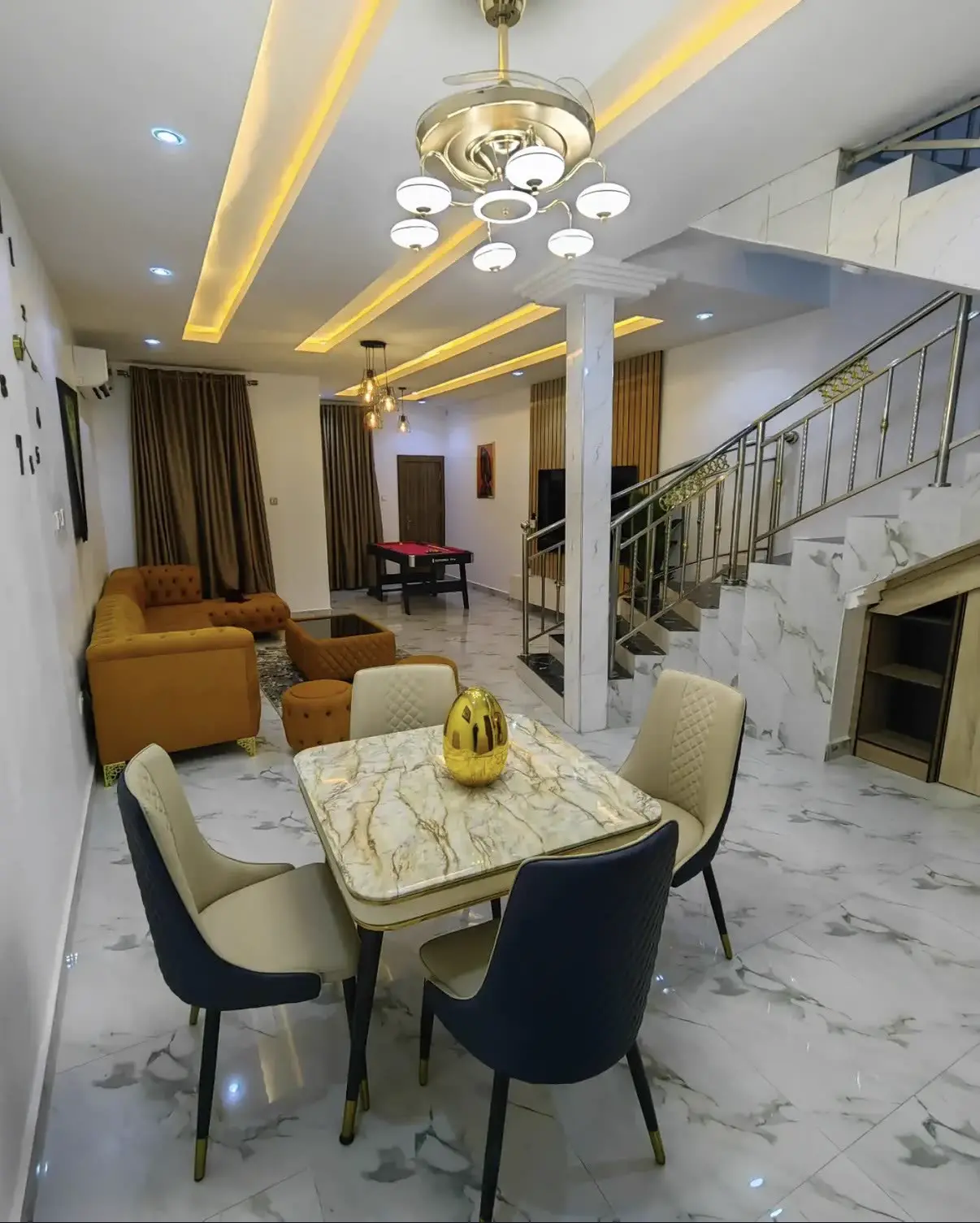 Open-plan living and dining room with marble floors, gold chandelier and velvet sofa
